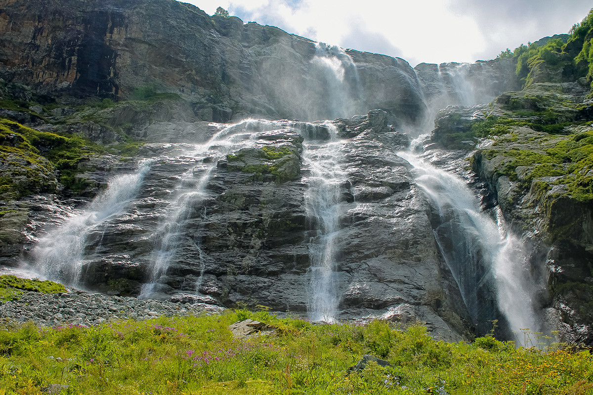 Sofia Waterfalls cascading into turquoise glacial lake surrounded by snow-capped peaks in Karachay-Cherkessia